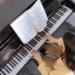 woman in yellow sweater playing grand piano with sheet music on the piano